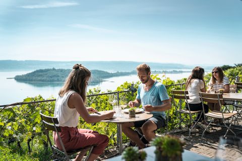 Ein Paar sitzt an einem Tisch in einem Restaurant mit Aussicht über den Bielersee und die St. Peterinsel. 