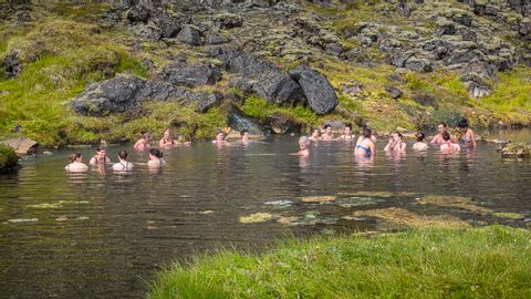 Personen die im Wasser baden, dahinter gleich ein begrünter Hügel