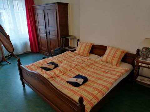Ein Zimmer im B&B Tilleul in Saint Imier. Ein Doppelbett aus Holz mit orangenem Bettbezug. 