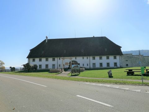 Ein Kloster in Bellelay steht bei strahlender Sonne auf einer grünen Wiese. Das Tête-de-Moine-Haus ist bekannt. 