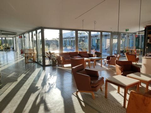 Die Lobby des Hotels in Gotland hat eine Fensterfront, durch die man in den Garten sieht. Die Lobby ist mit braunen Ledersesseln bestückt. 
