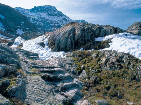 Von der Mitte nach links ist eine in den Fels gehauene Treppe, die an Steinhügeln und mit Schnee bedeckten stellen, vorbei zum Berg führt.