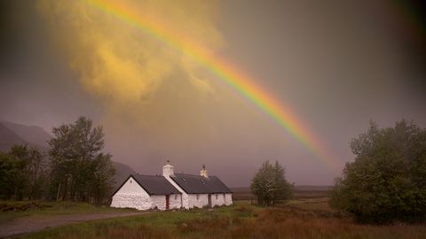 Ein Regenbogen zieht sich über ein weisses Haus auf der Wanderung auf dem West-Highland-Way in Schottland.
