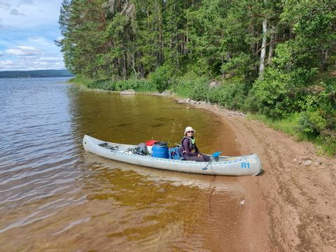 Eine Frau sitzt in einem Kanu am Ufer auf einem See in Schweden. 