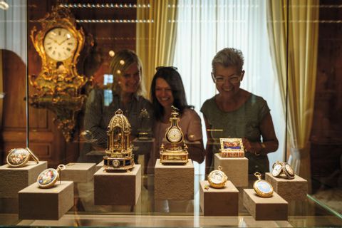 Drei Frauen sehen sich in Museum alte goldige Uhren an. 