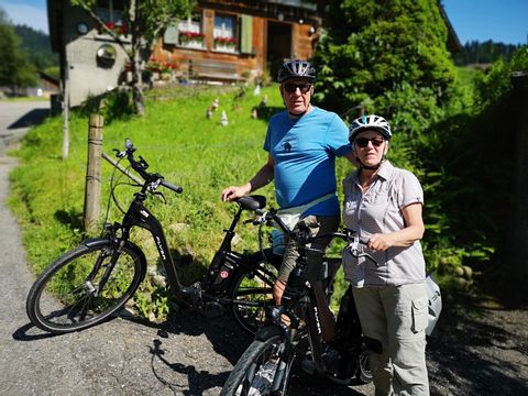 Zwei Radfahrer posieren vor einem traditionellen Haus auf ihrer Radtour. 