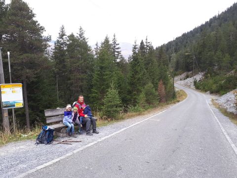 Wanderer sitzt mit drei Kindern auf der Bank an einer Bushaltestelle im Wald