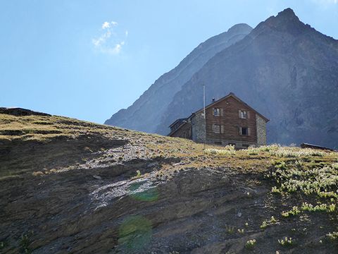 Eine einsame Hütte steht auf einem Hügel und ist umgeben von Bergen.
