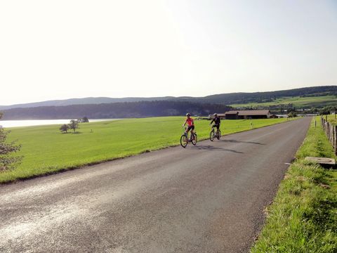 Piste cyclable dans la région du Jura avec vue sur le lac et les collines.