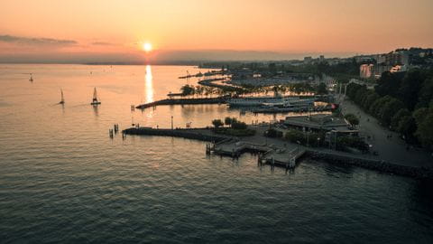 Die Sonne geht über dem Lac Léman unter und man sieht den Hafen von Lausanne. 