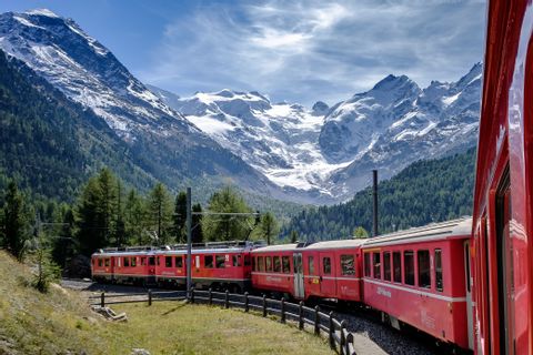The Rhaetian Railway travelling on the Bernina Pass with snow-covered mountains in the background.