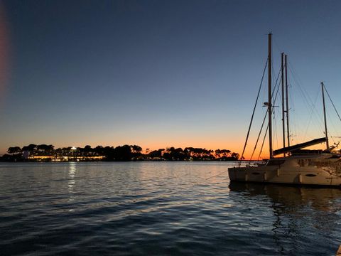 Man sieht den Sonnenuntergang am Pier in Porec und ein Katamaran auf der rechten Seite im Meer. 