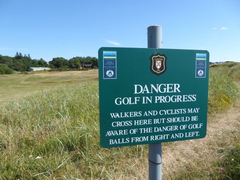 Ein grünes Schild am Wegesrand mit der Aufschrift: Vorsicht hier wird Golf gespielt. Auf gut Deutsch: Kopf einziehen!