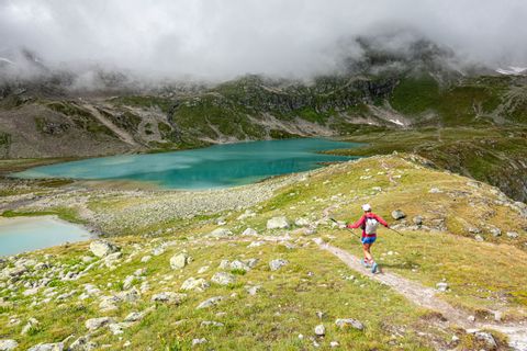 Trailrunner, welcher in die Richtung eines Bergsees rennt. Trailrunning Via Grischuna. Wanderferien mit Eurotrek.