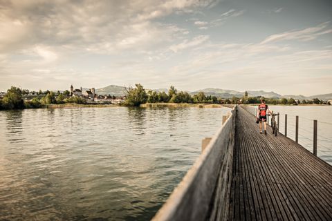 Un homme traverse un pont en bois qui mène à la vieille ville de Rapperswil. La route du cœur. Vacances à vélo avec Eurotrek.
