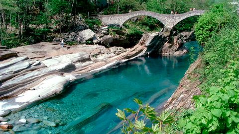 Eine Bogenbrücke unter der ein Fluss mit klarem türkisblauem Wasser durchfliesst. Sentiero Verzasca. Wanderferien mit Eurotrek.