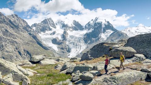 Ein Wanderer-Pärchen läuft über ein Steinplateu. Im Hintergrund ,die Gletscherzungen die kurvig vom Berg hinunter führen.