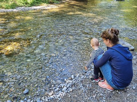 Andrea steht mit ihrem Sohn an einem Fluss und schaut aufs Wasser. 