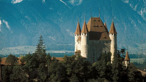 The tower of Thun Castle behind a small piece of forest, and in front of the mountains.