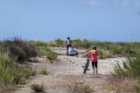 Zwei Radfahrer mit einem Kinderanhänger an einem Strandabschnitt auf Sardinien