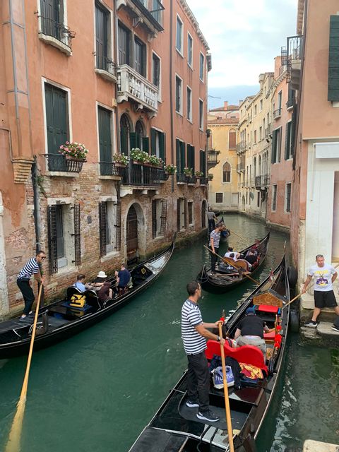 Durch einen kleinen Kanal in Venedig fahren zwei Gondoliere aneinander vorbei. 