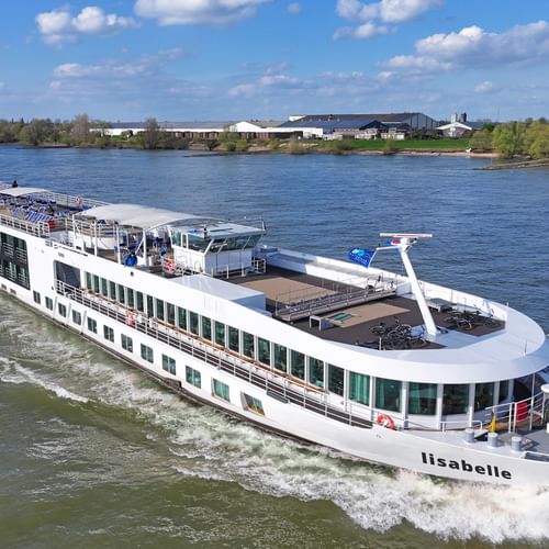 Weißes Flusskreuzfahrtschiff MS Lisabelle fährt auf blauem Wasser mit Kielwasser dahinter. Das Schiff hat mehrere Decks und grün getönte Fenster.