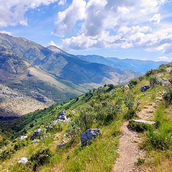 Spektakulärer Balkan-Bergwanderweg Ausblick Gewundener Wanderweg durch felsiges Gelände im Balkan mit spektakulärem Blick auf Bergtal unter bewölktem blauen Himmel.