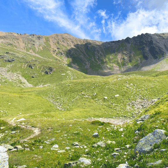 Eine Wanderin schaut zum Berg hinauf von einer grünen Wiese auf dem Mittelbündner Panoramaweg.