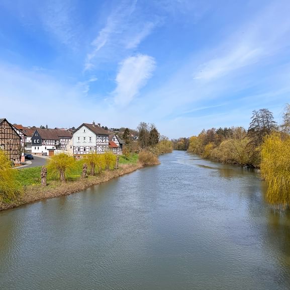 Die Lahn fließt ruhig durch eine deutsche Stadt mit traditionellen Fachwerkhäusern und modernen Gebäuden entlang der Ufer unter blauem Himmel.