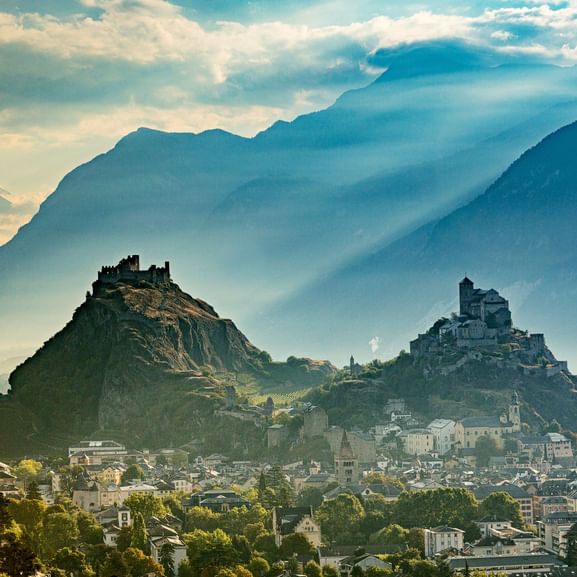 Vue panoramique de Sion, Suisse avec deux collines rocheuses surmontées de ruines de châteaux et d'une église dominant la ville.
