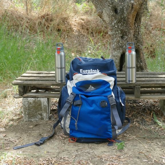 Sac à dos de randonnée Eurotrek bleu et blanc sur banc en bois avec deux bouteilles d'eau en acier inoxydable à Zakynthos.