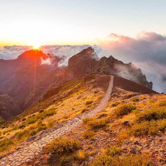 Sentier de randonnée en pierre serpentant à travers un paysage montagnard doré au lever du soleil au Portugal.
