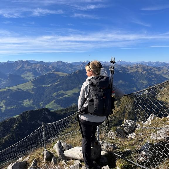 Wanderin mit Rucksack und Wanderstöcken steht am felsigen Gipfel-Aussichtspunkt auf dem Stockhorn mit Blick auf Alpentäler und Bergketten.