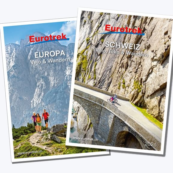 Deux catalogues Eurotrek 2026 : l'un montre des randonneurs en montagne 'Europa Velo & Wandern', l'autre un cycliste sur pont en pierre 'Schweiz'.