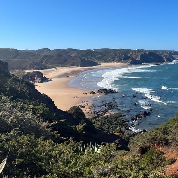 Weitlaeufiger Sandstrand mit Wellen und Felsen