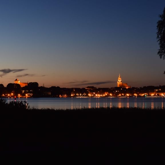 Die Beleuchtete Stadt am Seeufer in der Abenddämmerung. Die lichter spiegeln sich im See.