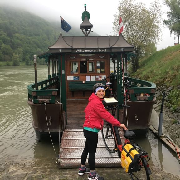 Maria-Teresa in roter Jacke und Fahrradhelm beim Besteigen eines traditionellen Donauschiffs mit ihrem Velo auf der Gangway.