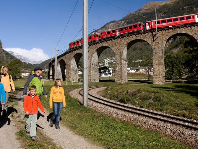 Fünf Wanderer bestauenen die Fahrt der Rhätischen Bahn über ein Viadukt in Brusio in der Region Bernina im Kanton Graubünden.