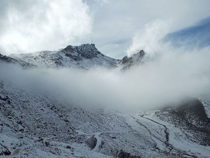Eine traumhafte Winter-Berglandschaft. Der Berg ist Schneebedeckt und unter den^m Spitz zieht eine weisse Wolke vorbei.