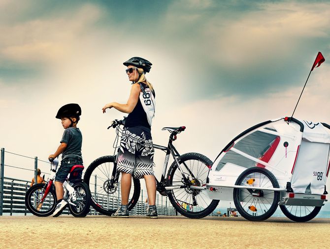 Eine Mami mit Kinderanhänger in ihrem Bike und der Sohnemann mit seinem Laufrad machen eine kurze Pause.