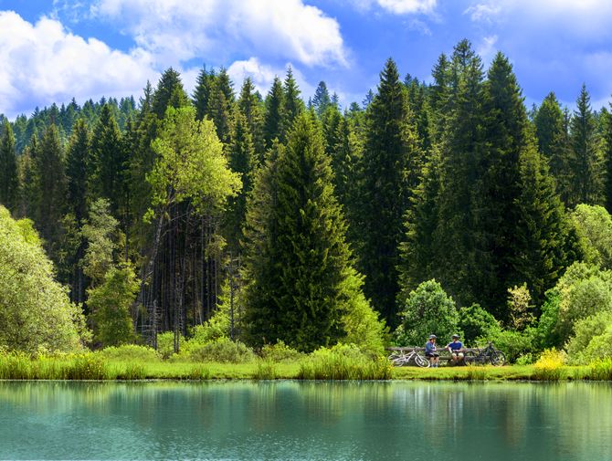 Zwei Velofahrer geniessen die Ruhe an dem ruhigen Ufer des Sees in den unberührten Wäldern im Kanton Jura.
