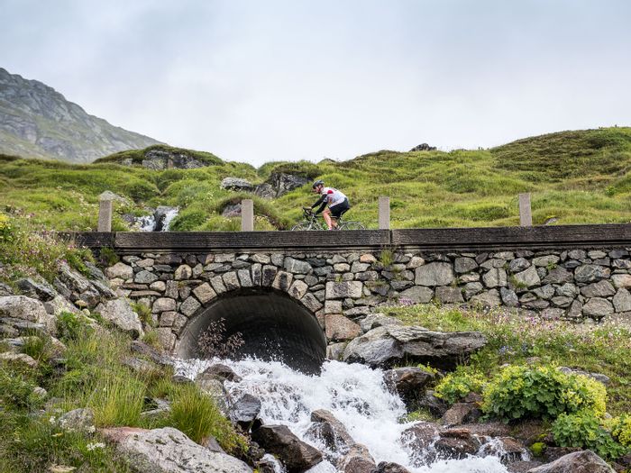 A biker rides over a stone bridge where water flows through an arch.