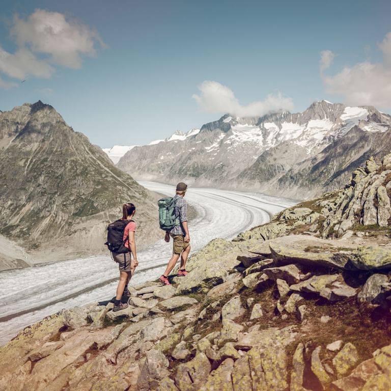 Deux randonneurs marchent près du glacier d'Aletsch sur un chemin caillouteux.
