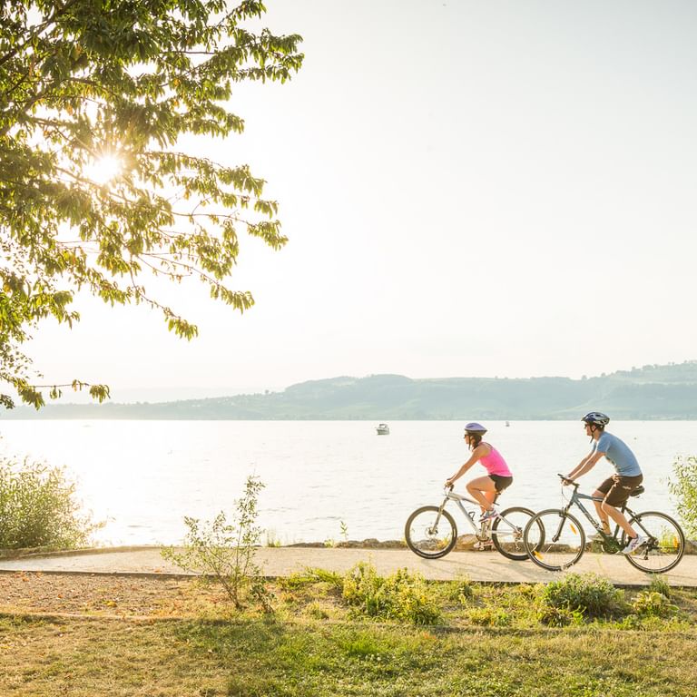Zwei Radfahrer fahren gemütlich dem Ufer des Murtensees entlang. Jura-Route. Veloferien mit Eurotrek.