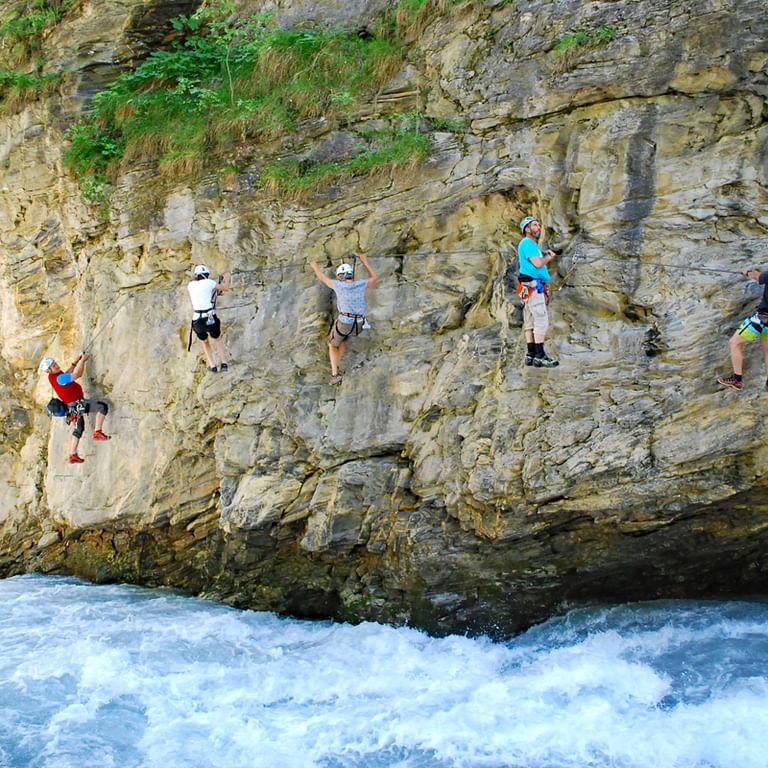 Sechs Kletterer mit Helmen und Gurten erklimmen eine hohe Kalksteinwand über rauschenden weißen Gewässern in Tirol, Österreich.