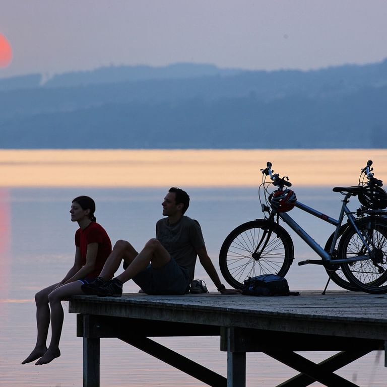 Velofahrer, die den Sonnenuntergang auf einem Steg geniessen Velofahrer, die den Sonnenuntergang auf einem Steg geniessen. Aare-Route. Veloferien mit Eurotrek.