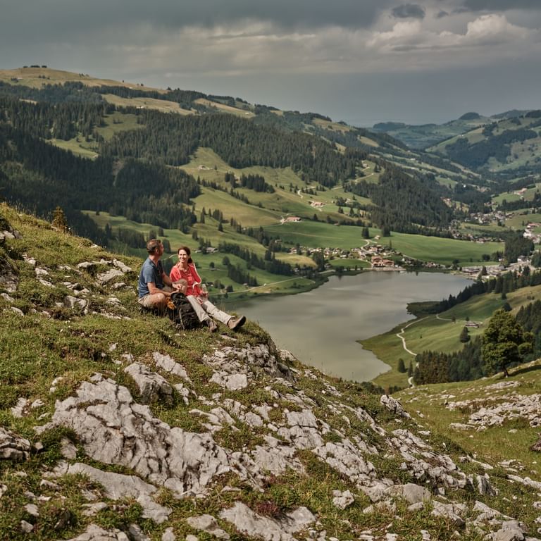 A man and a woman sitting on a hill overlooking a lake